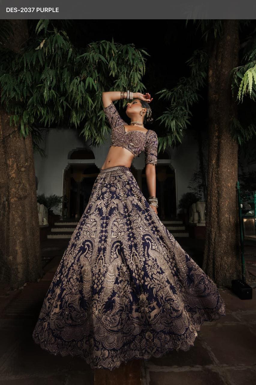 Woman wearing a deep purple raw silk lehenga with heavy gold zardozi embroidery featuring peacock motifs and matching elbow-sleeve blouse, posing outdoors at night