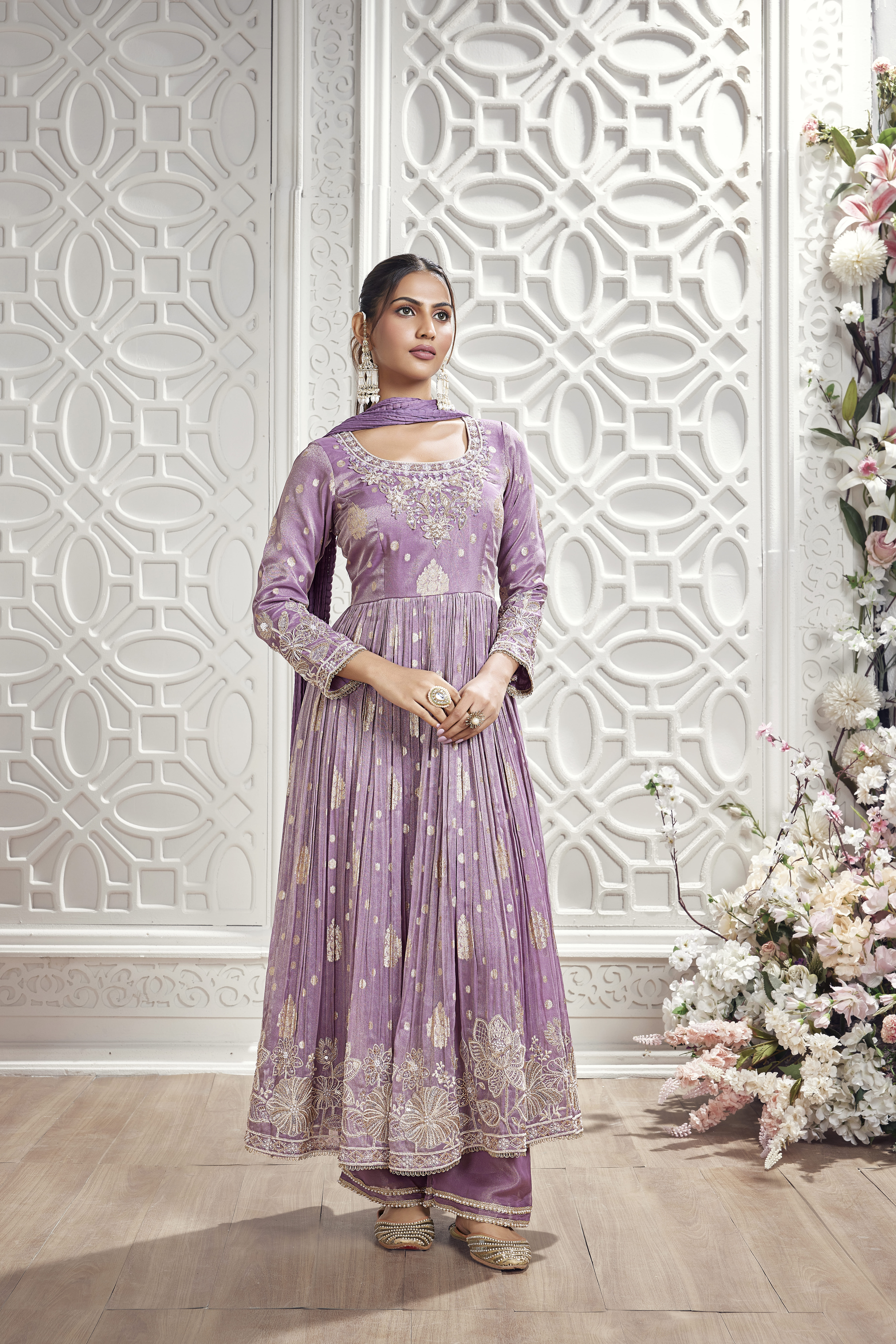 Model wearing a lavender embroidered Anarkali suit with matching pants and dupatta in a luxurious floral-inspired interior setting.