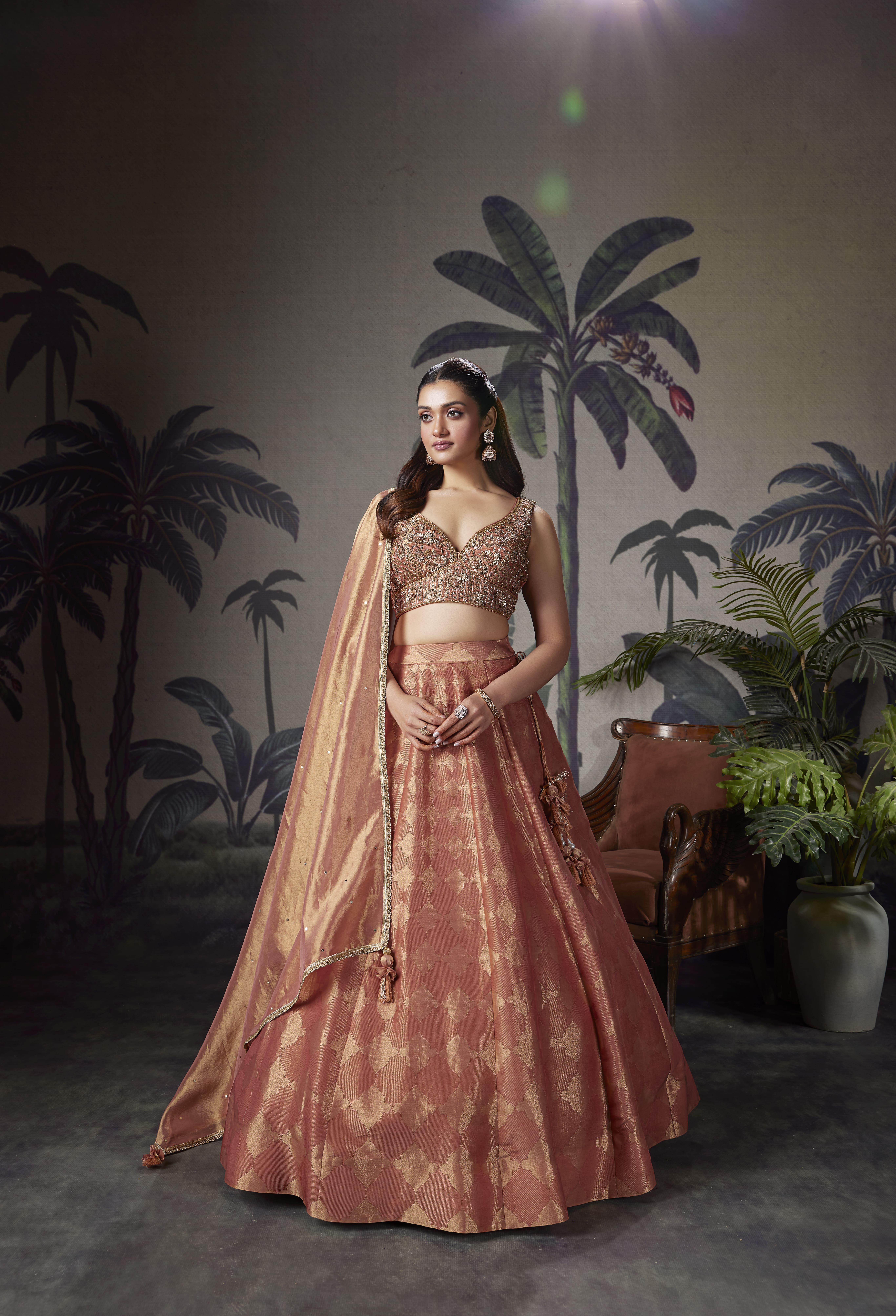 Model wearing a rose gold Banarasi silk lehenga with embroidered sleeveless blouse and matching dupatta featuring zari detailing.
