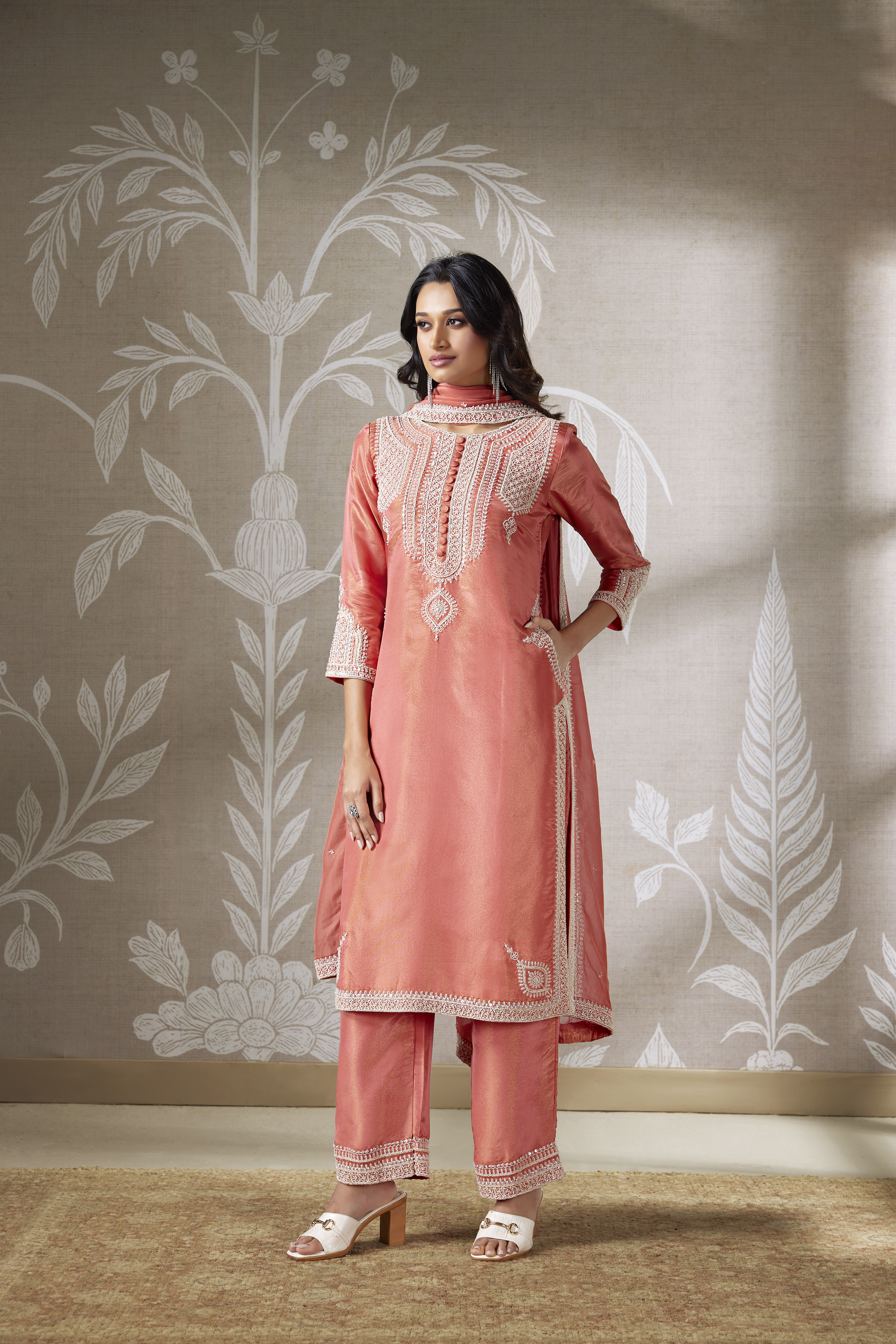 Woman wearing a peach coral embroidered silk kurta set with matching straight pants and dupatta.