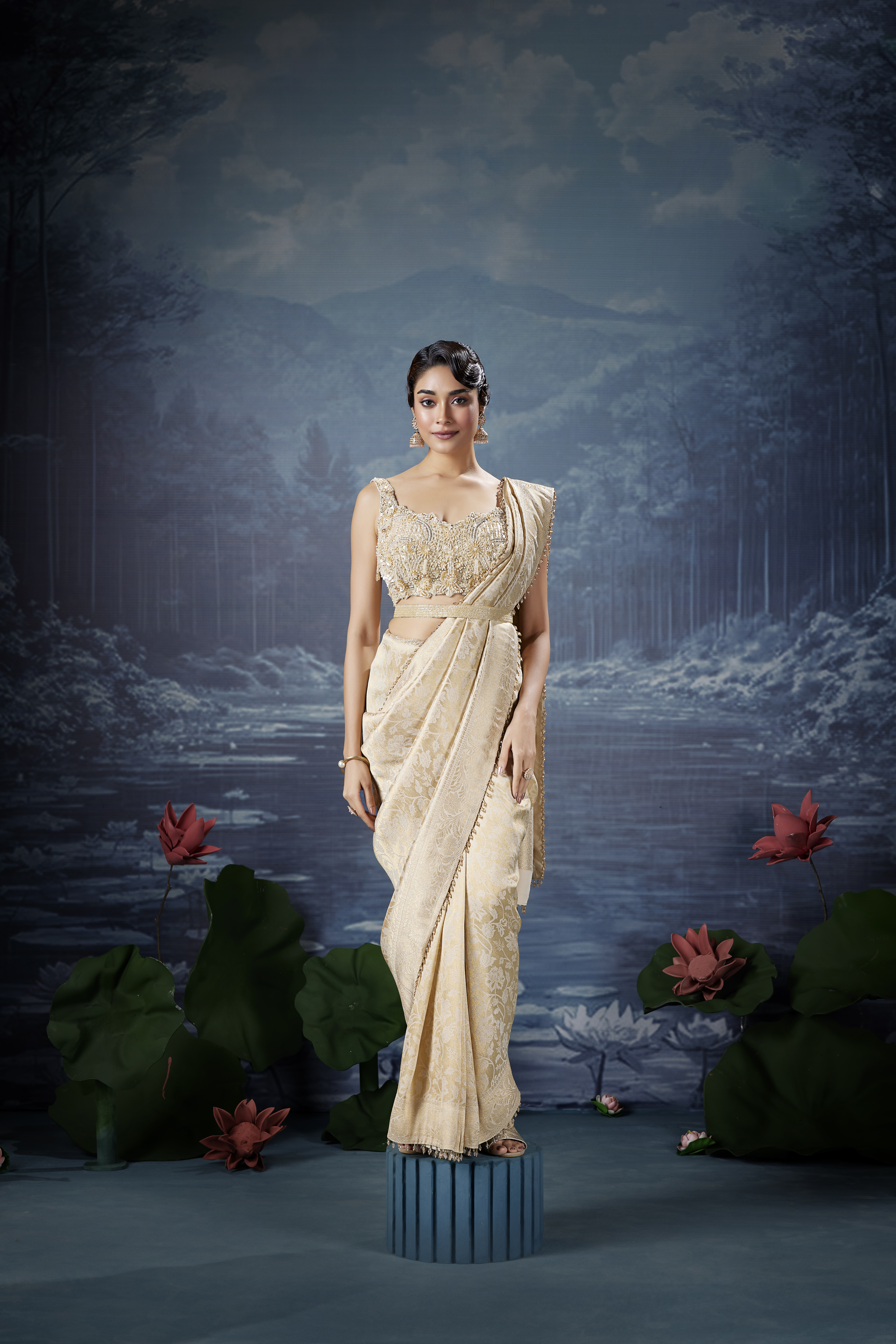 Model wearing an ivory embroidered designer saree with an embellished blouse, posing against a dreamy lotus lake backdrop.