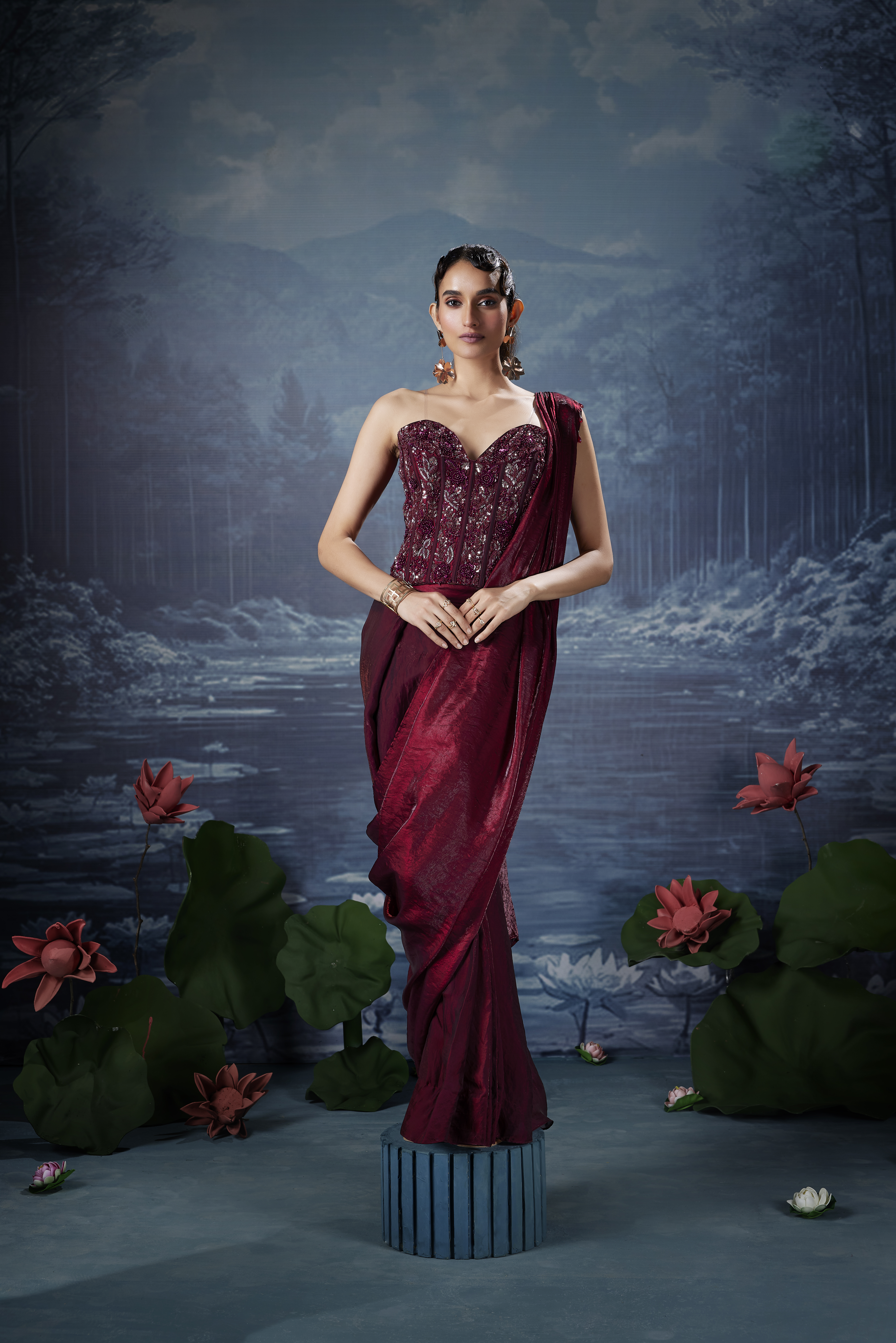 Woman wearing deep wine red designer saree with embellished corset blouse, modern one shoulder drape saree look with elegant evening styling
