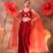 Woman wearing a ruby red embroidered blouse with attached sheer cape sleeves and a satin drape skirt, posing against a backdrop with large red flowers