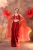 Woman wearing a ruby red embroidered blouse with attached sheer cape sleeves and a satin drape skirt, posing against a backdrop with large red flowers