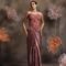 Woman wearing a mauve satin drape gown with a strapless sheer corset bodice featuring floral embroidery and crystal tassels, posing against a backdrop with large blush flowers