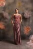 Woman wearing a mauve satin drape gown with a strapless sheer corset bodice featuring floral embroidery and crystal tassels, posing against a backdrop with large blush flowers