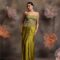 Woman wearing an olive green satin drape gown with a heavily embellished 3D floral corset top and spaghetti straps, posing against a backdrop with large pastel flowers