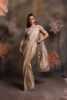 Woman wearing a champagne gold pre-draped satin saree with crystal border and a silver embellished halter-neck blouse, posing against a floral backdrop