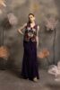 Woman wearing an aubergine purple flared pants set with matching bustier and a sleeveless jacket featuring 3D floral embroidery in red and pink, posing against a floral backdrop