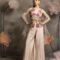 Woman wearing an ivory satin palazzo set with a sleeveless jacket featuring 3D floral embroidery in pink and orange, and a sheer organza dupatta, posing against a floral backdrop